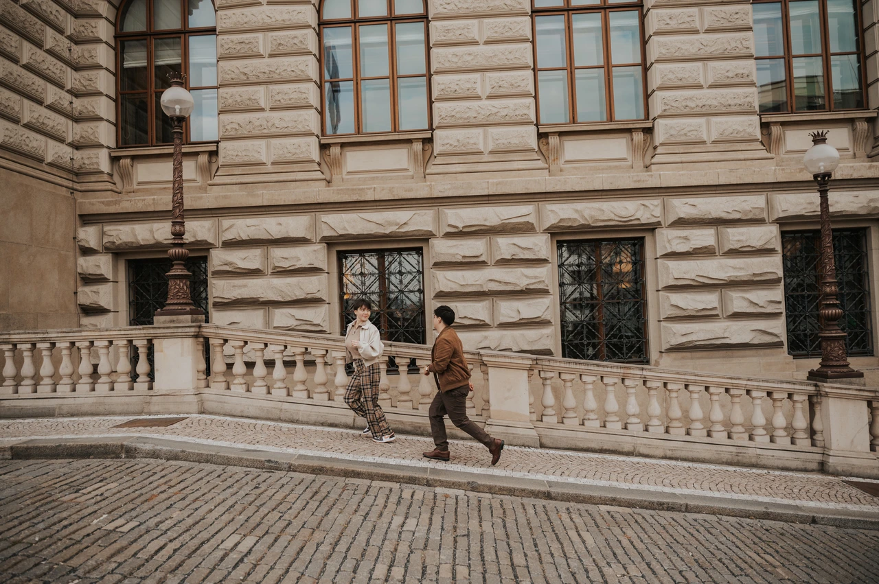 Prague couple photoshoot: couple strolling past the ornate museum windows. Couple strolling past the ornate museum windows during a couple photoshoot in Prague.