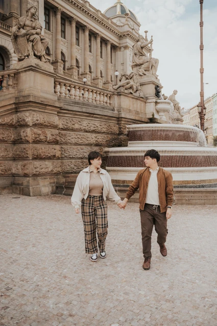 Prague couple photoshoot: couple walking hand in hand past the National Museum fountain. Couple walking hand in hand past the National Museum fountain during a couple photoshoot in Prague.