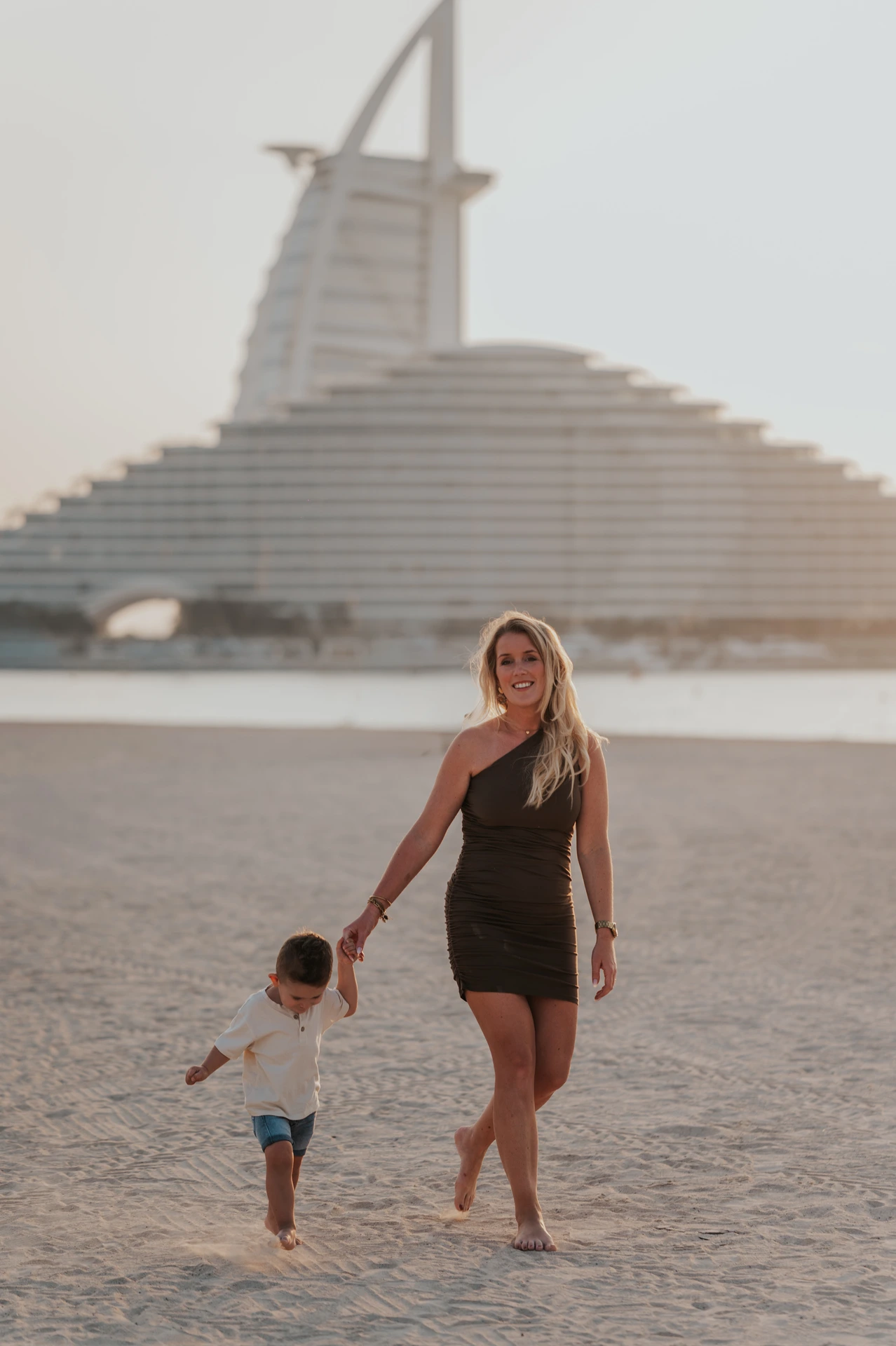 Family beach photoshoot locations Dubai - mother portrait A mother stands on Dubai beach with Jumeirah Beach Hotel in the background during a family beach photoshoot.