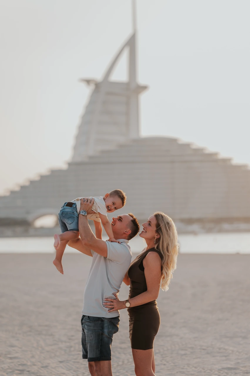 Family beach photoshoot locations Dubai - parents lifting toddler Parents lift their toddler in the air on Dubai beach near Jumeirah Beach Hotel during a joyful family beach photoshoot.