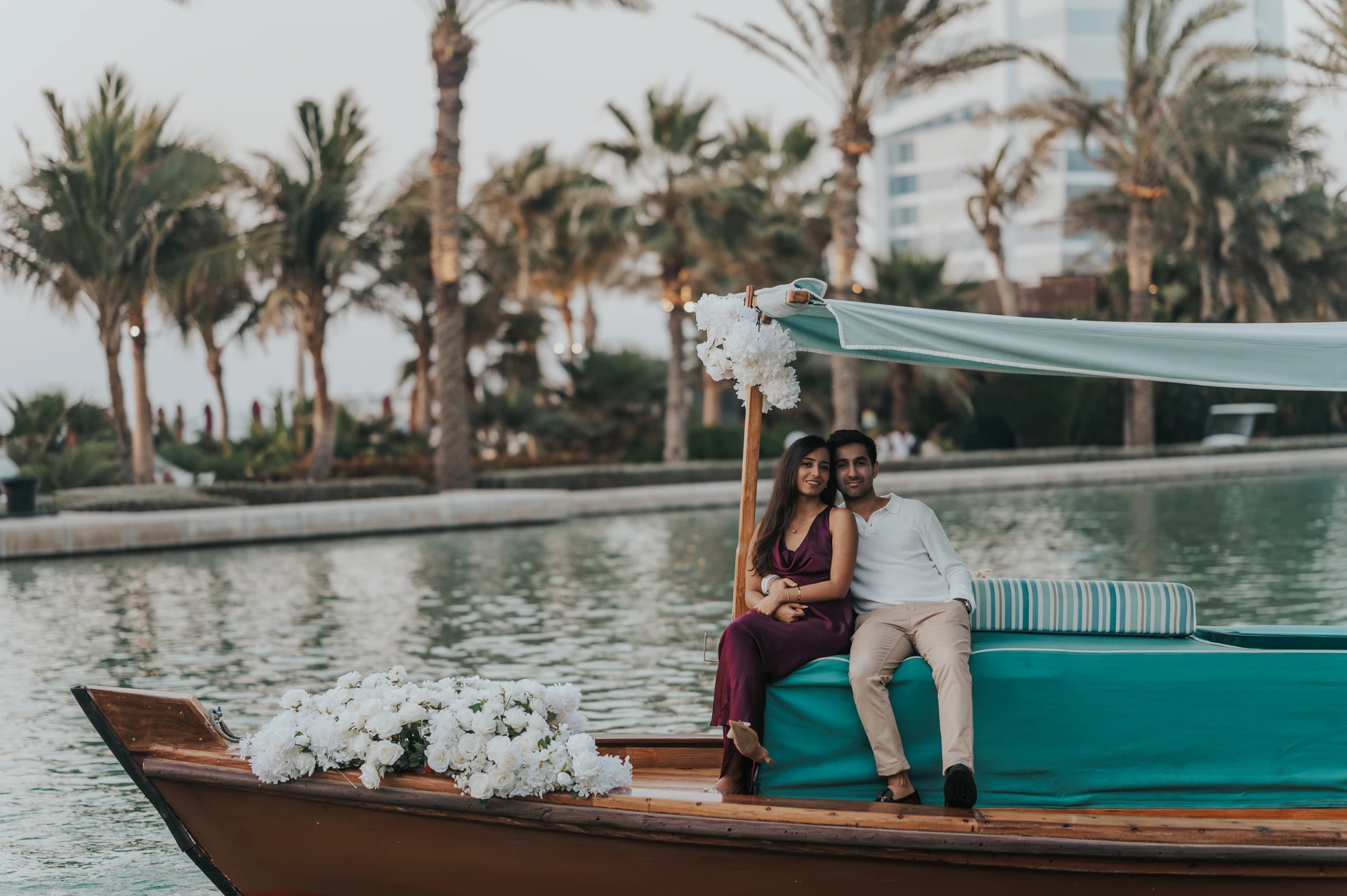 A couple sits on a decorated abra in Dubai with flowers around them, showing a styled proposal setup by the water during a proposal photoshoot.