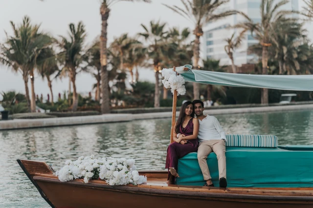 A couple sits on a decorated abra in Dubai with flowers around them, showing a styled proposal setup by the water during a proposal photoshoot.