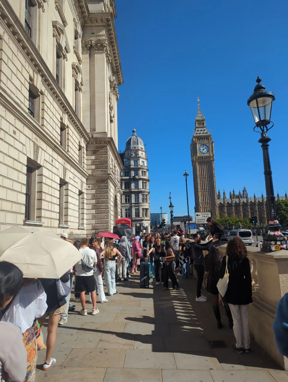 Busy Westminster pavement with people beside a red telephone box and Elizabeth Tower in the background