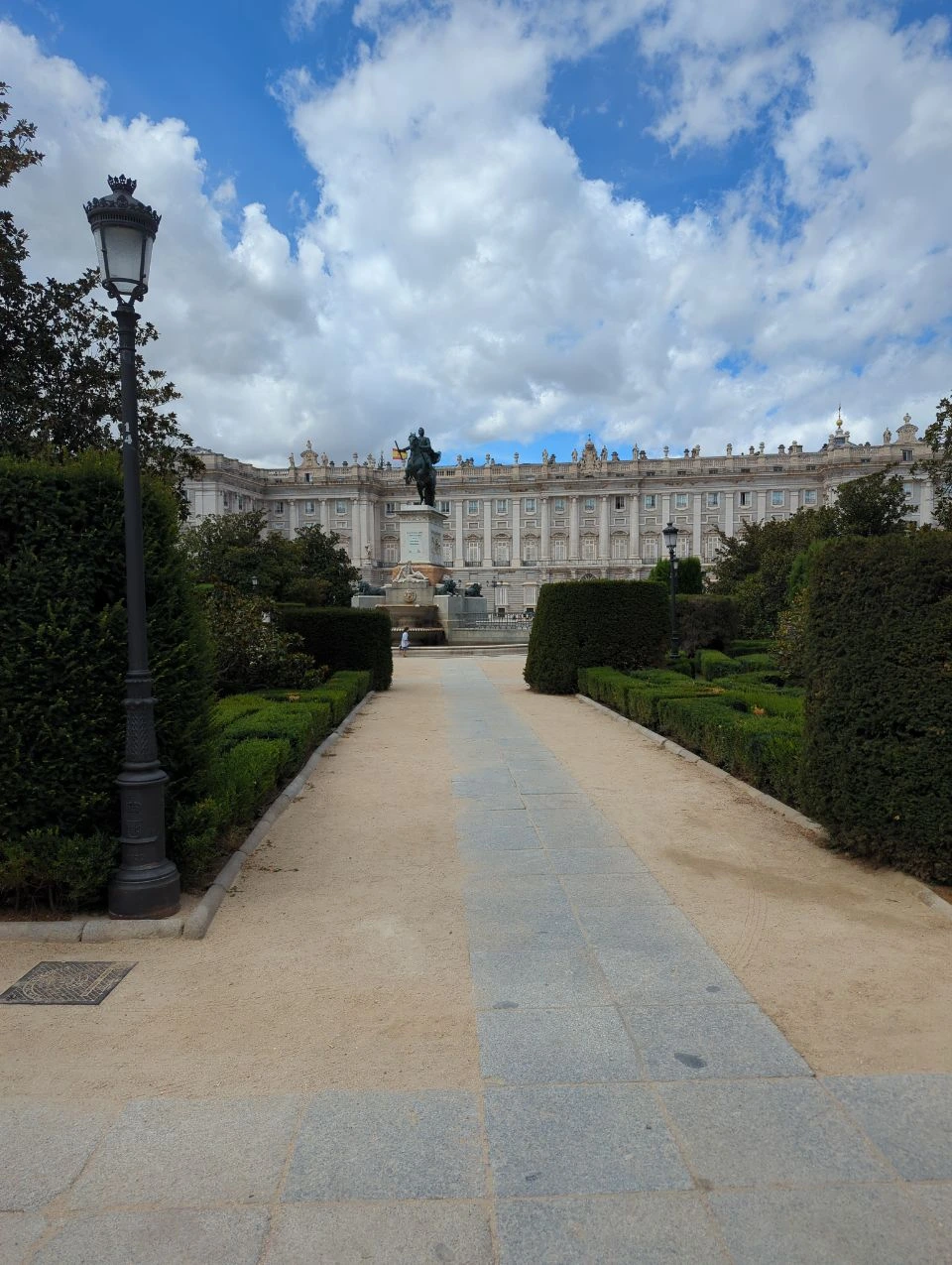The Royal Palace rises behind clipped hedges and an equestrian statue at a Plaza de Oriente photoshoot setting in Madrid.