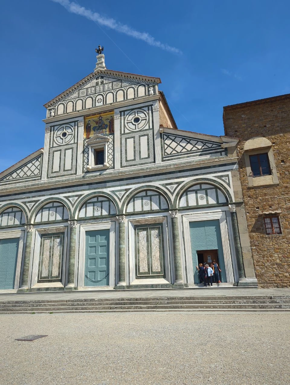 San Miniato al Monte Architecture The patterned marble facade and broad forecourt of San Miniato al Monte stand beneath a clear blue sky.