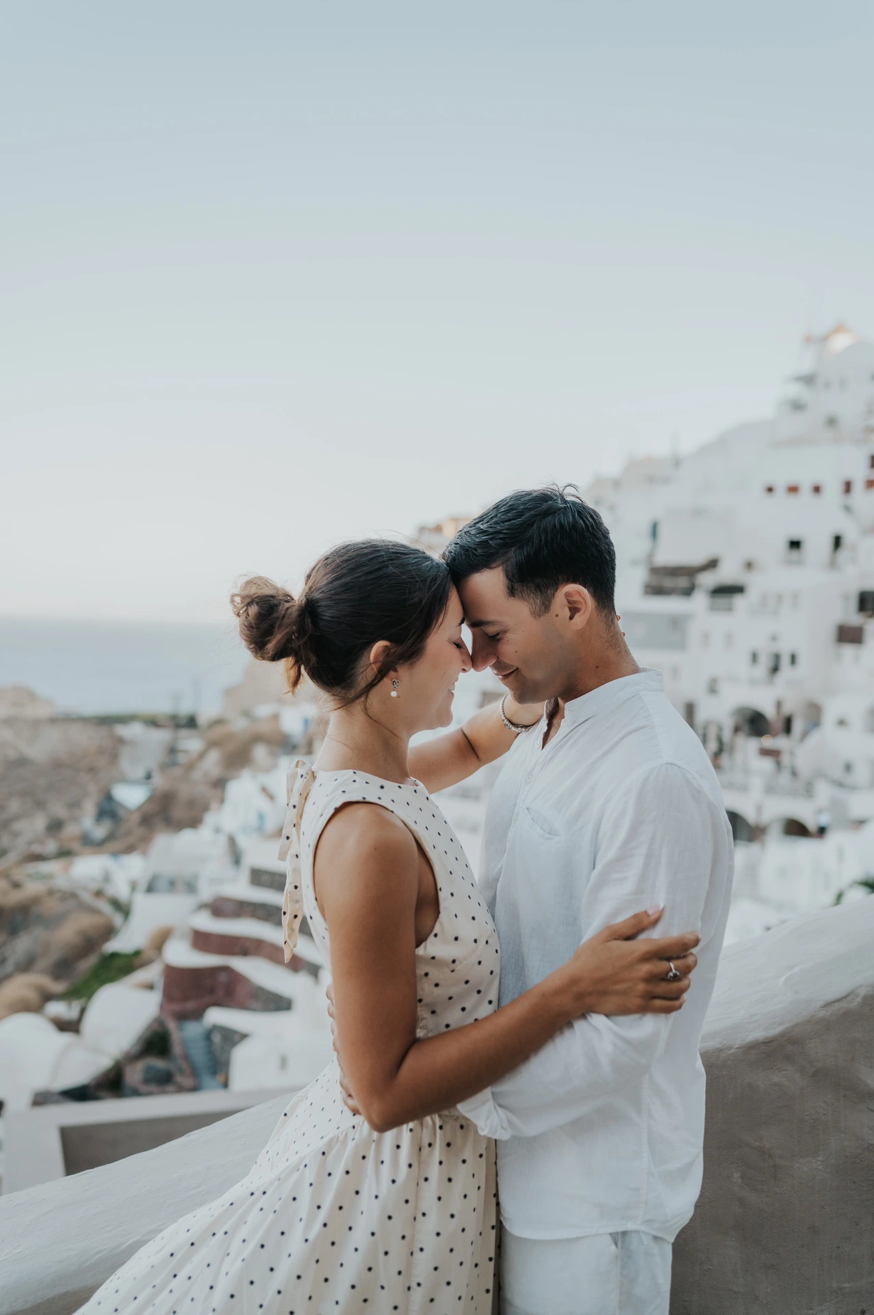 Close portrait of a couple kissing with white hillside buildings behind them during their Santorini couple photoshoot.