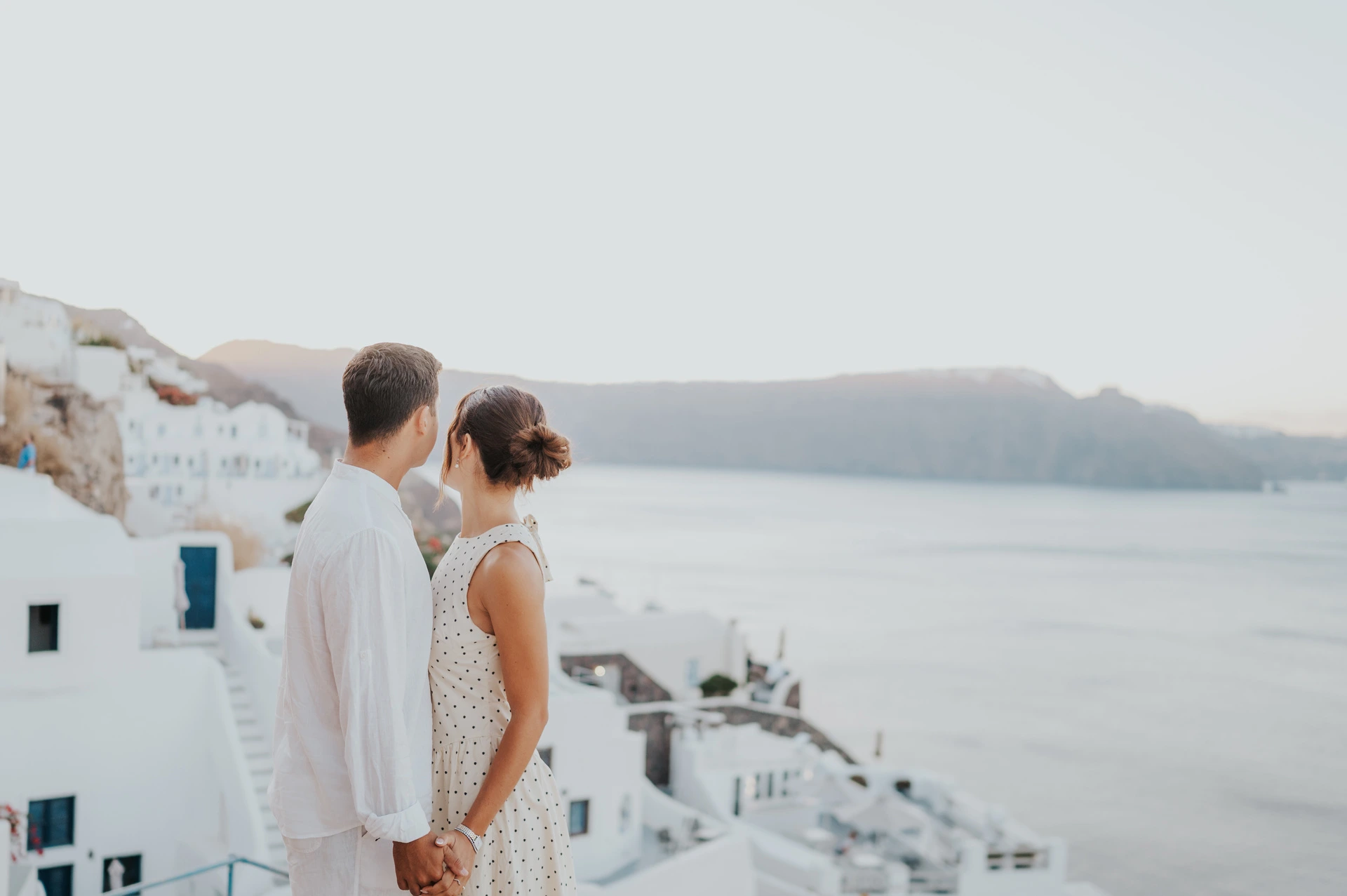 Couple seen from behind looking across the sea from a white village terrace during their Santorini couple photoshoot.