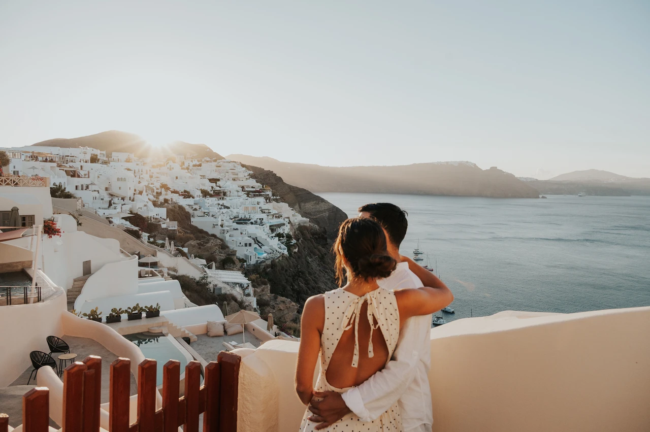 Santorini couple photoshoot: portrait in a polka-dot dress above the sea Woman in a cream polka-dot dress looking across the white village and sea during their Santorini couple photoshoot.