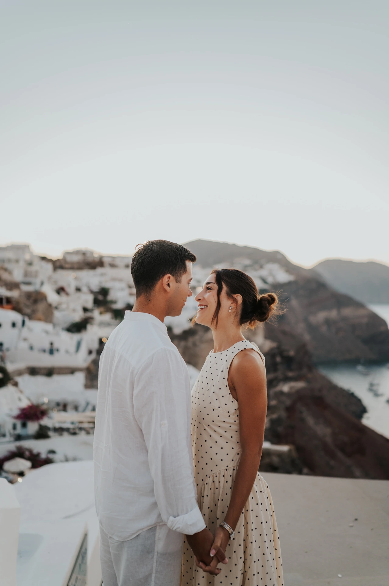 Portrait of a couple facing one another above a white village and the caldera during their Santorini couple photoshoot.