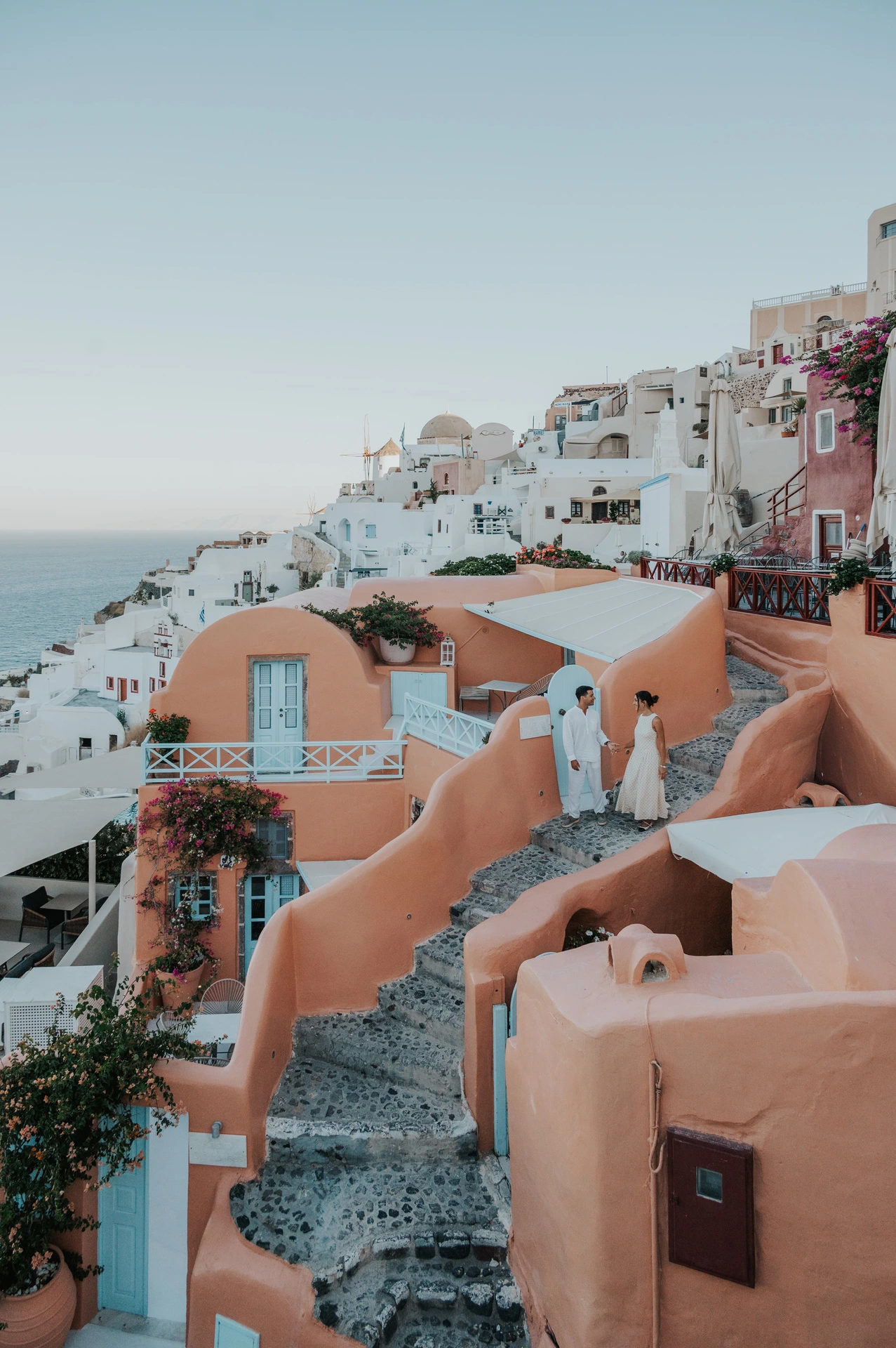 Couple walking along winding cobbled steps between peach-coloured walls during their Santorini couple photoshoot.