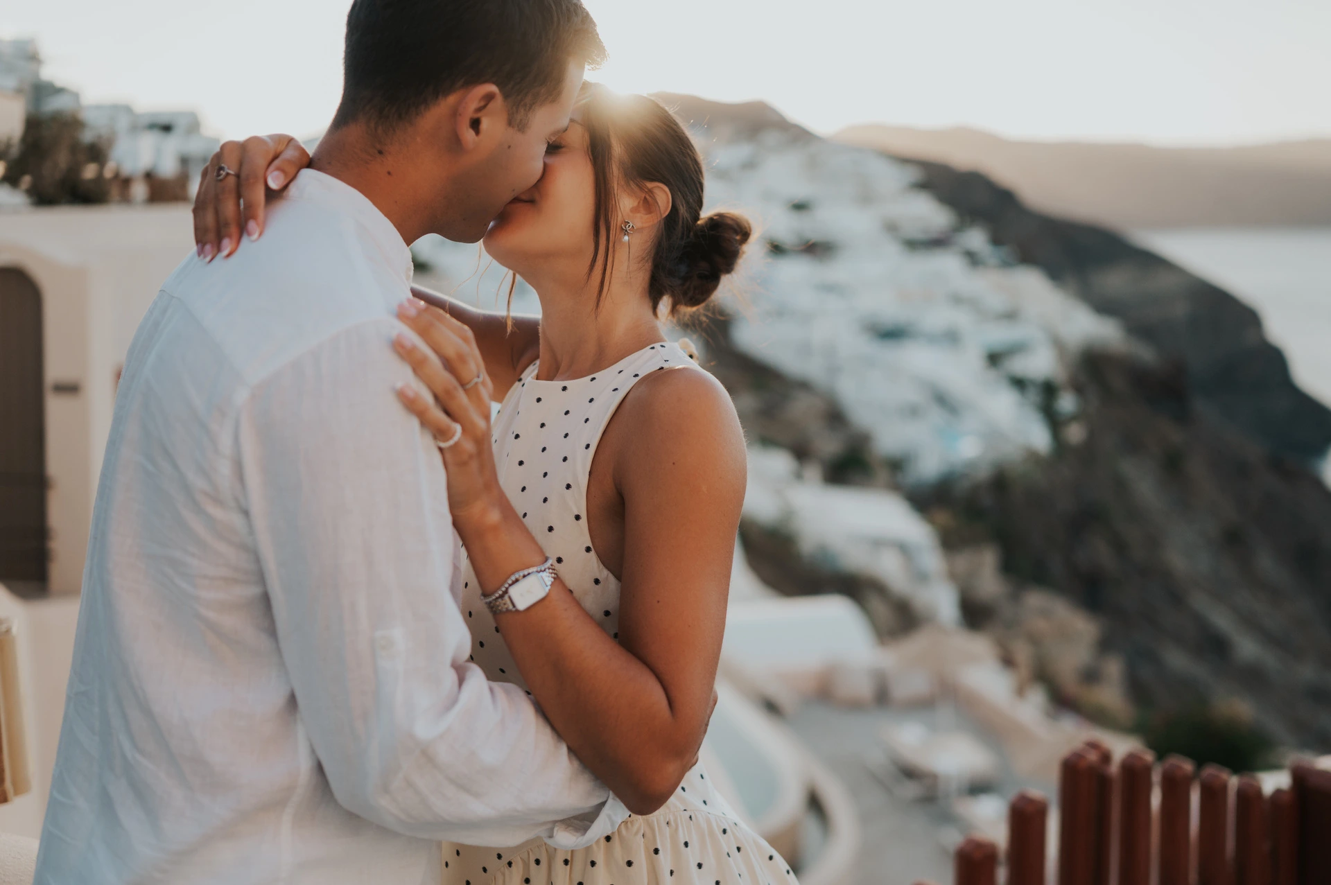 Close portrait of a couple kissing with warm light over the white village and caldera during their Santorini couple photoshoot.