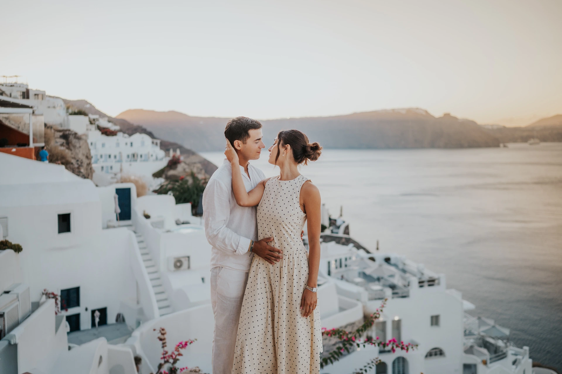 Couple facing each other above white rooftops with warm light across the sea during their Santorini couple photoshoot.