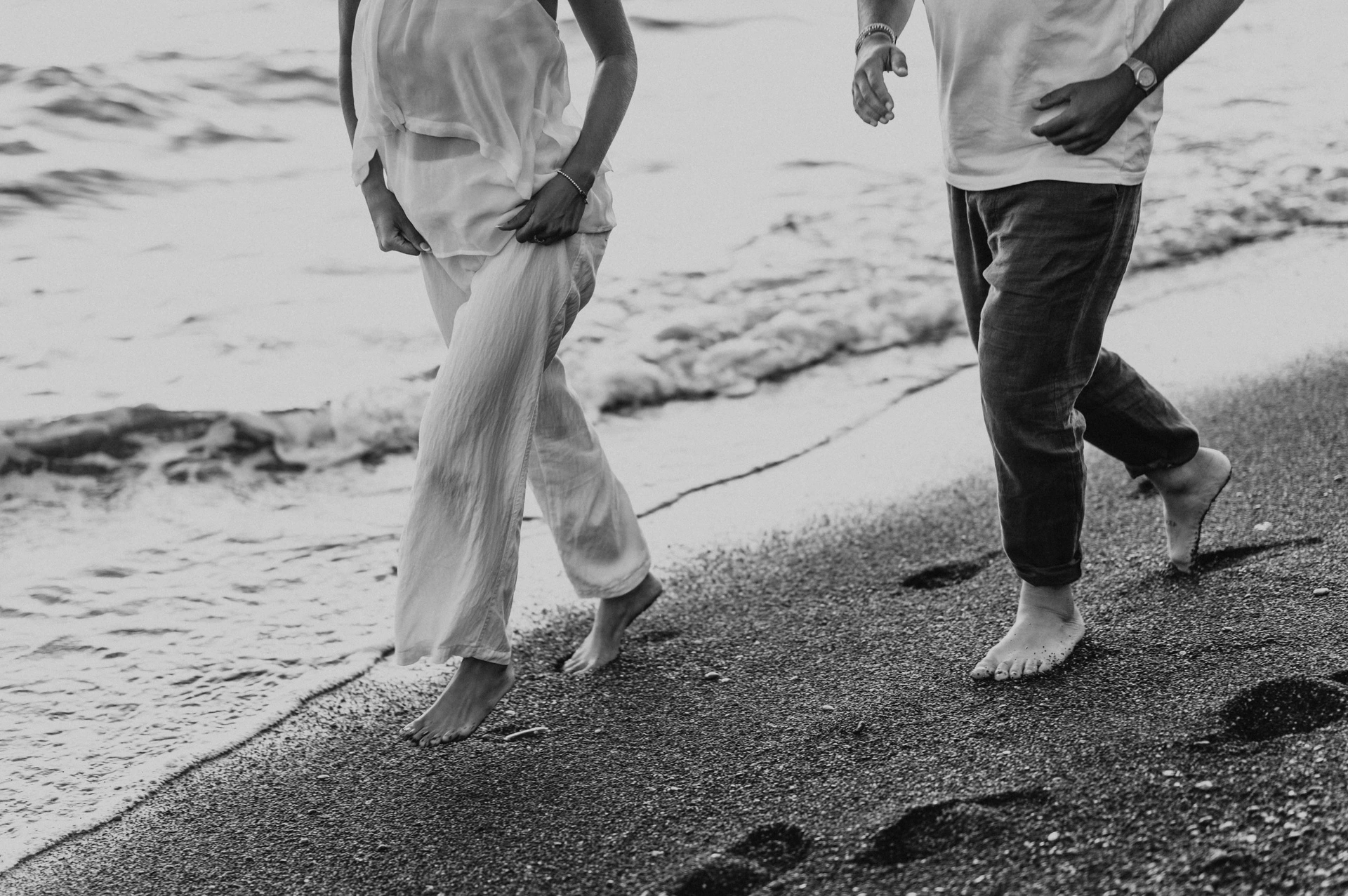 Black-and-white detail of a couple’s bare feet moving across the dark beach during their Santorini couple photoshoot.
