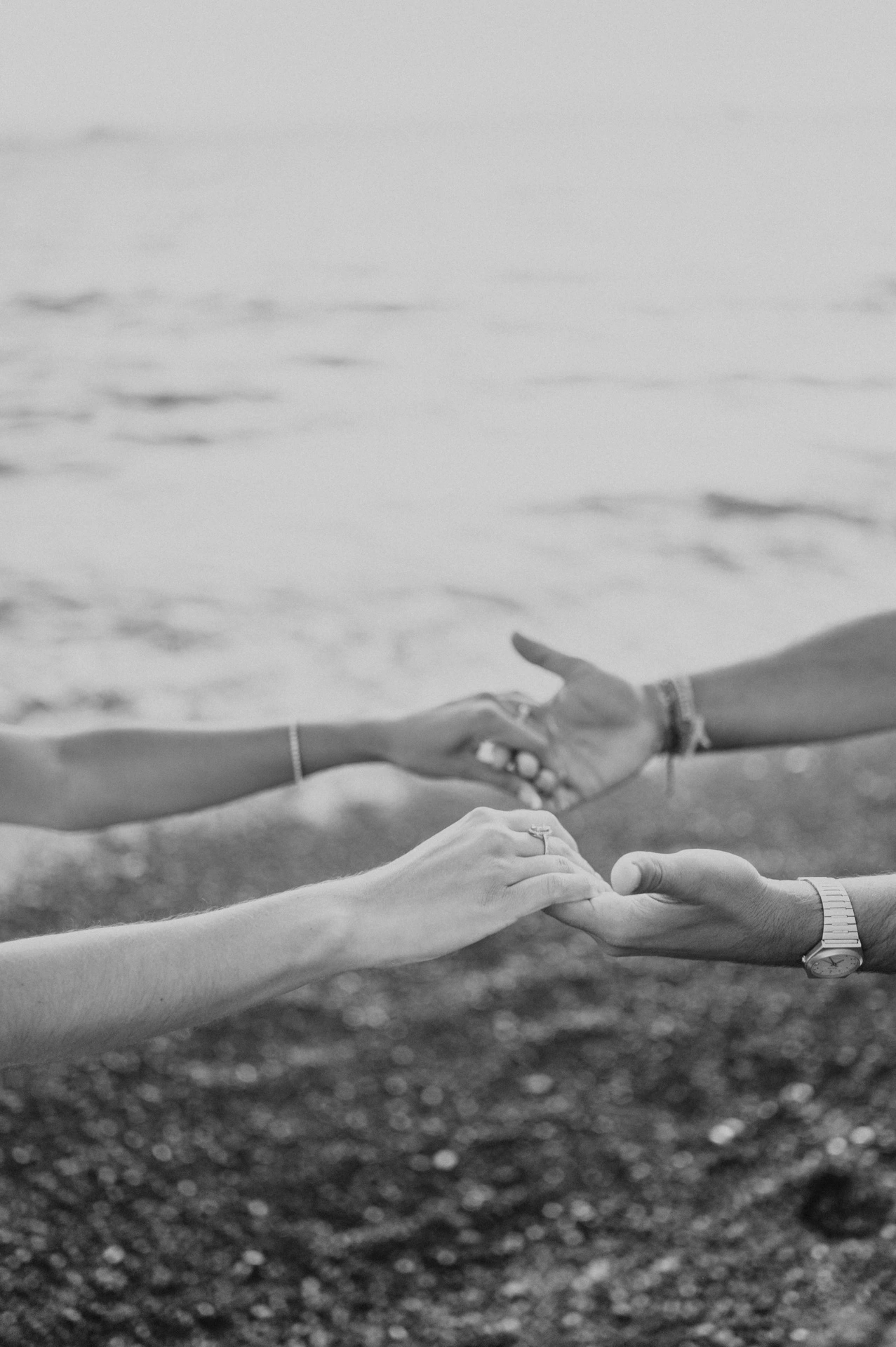 Black-and-white close-up of a couple’s joined hands beside the sea during their Santorini couple photoshoot.
