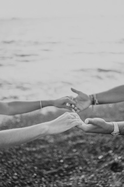 Santorini couple photoshoot: black-and-white detail of joined hands Black-and-white close-up of a couple’s joined hands beside the sea during their Santorini couple photoshoot.