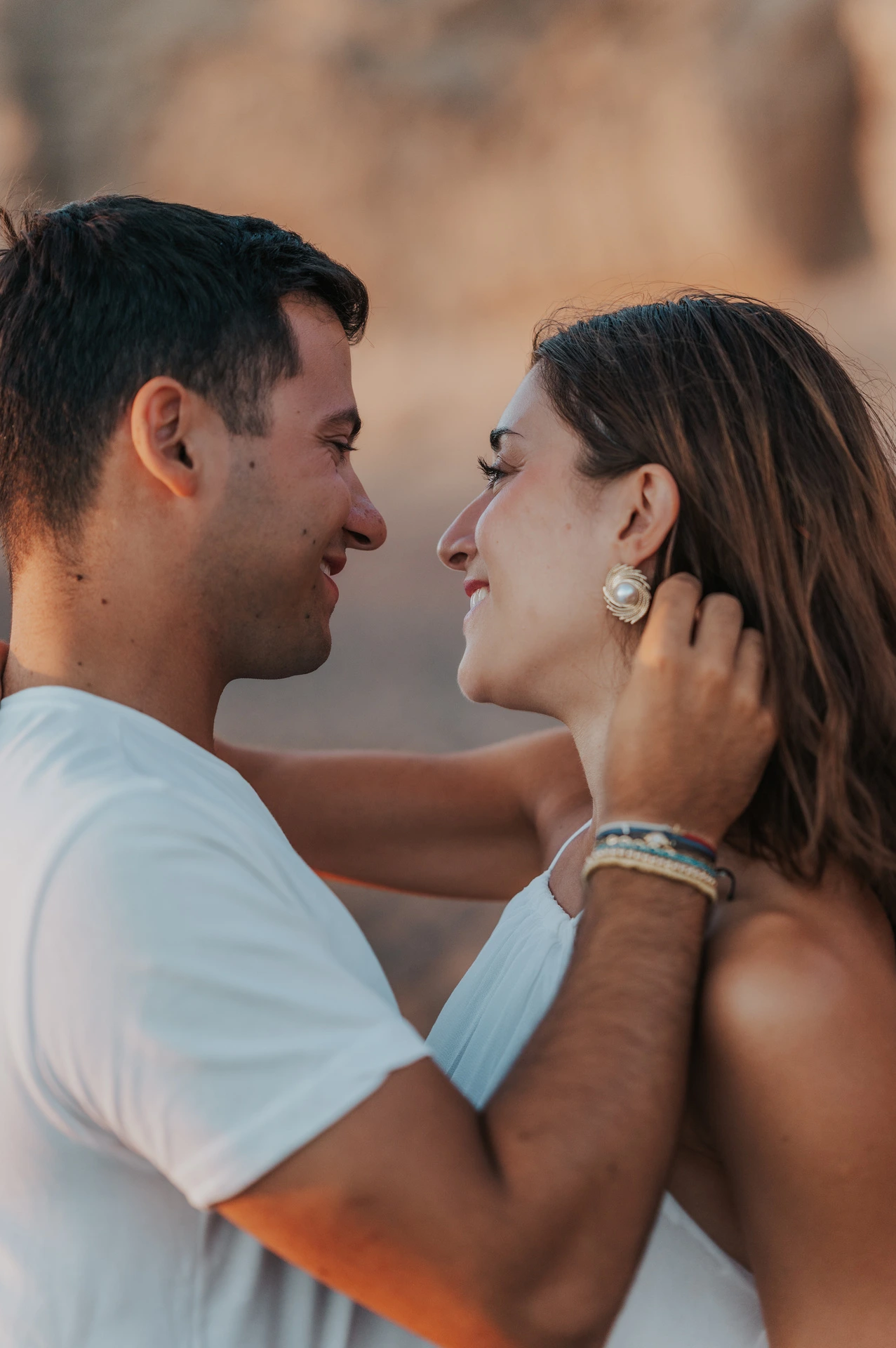 Close portrait of a couple smiling at each other beside Vlychada’s pale cliffs during their Santorini couple photoshoot.