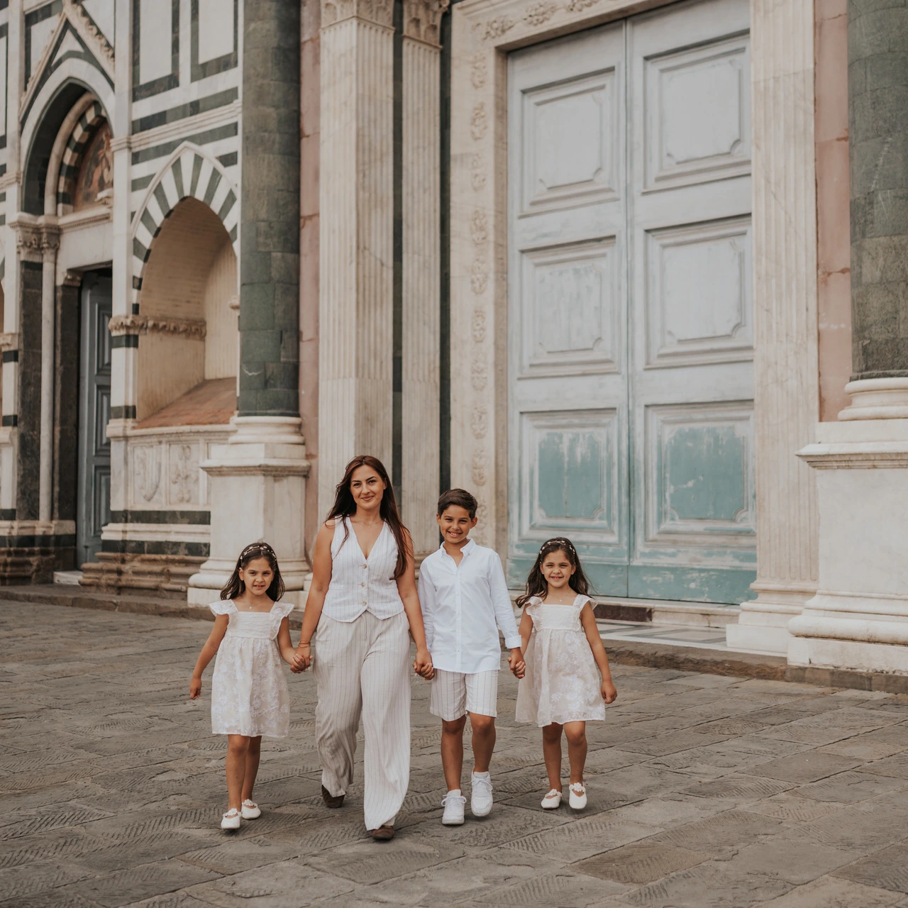 Una donna cammina con tre bambini davanti a porte di chiesa in marmo decorato durante un servizio fotografico di famiglia a Firenze.
