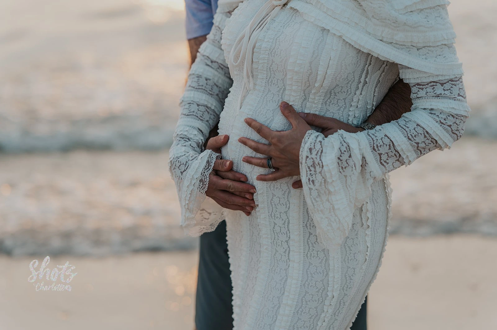 Close-up delle mani della coppia appoggiate sul pancione durante un servizio fotografico di gravidanza sulla spiaggia di Dubai.