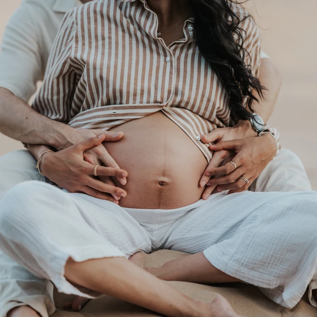servizio fotografico gravidanza Dubai Coppia in dolce attesa seduta sulla sabbia che tiene il pancione durante un servizio fotografico di gravidanza nel deserto di Dubai.