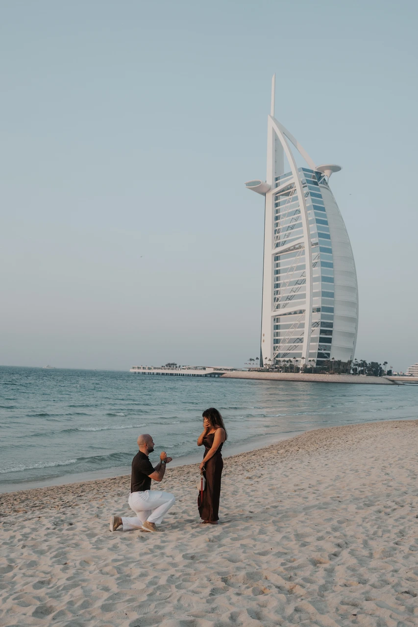 Proposal at Shimmers - quiet shoreline portrait A woman sits near the waterline by Shimmers in Dubai during a proposal session portrait, with Burj Al Arab and sea behind her.