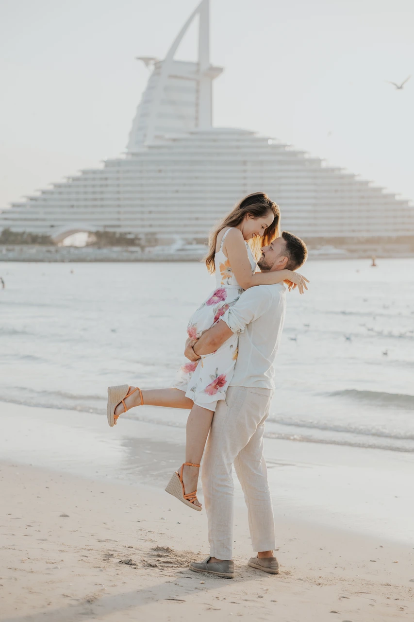 Backup kit that saves engagement photo sessions Couple lifting pose on beach near Burj Al Arab during engagement session