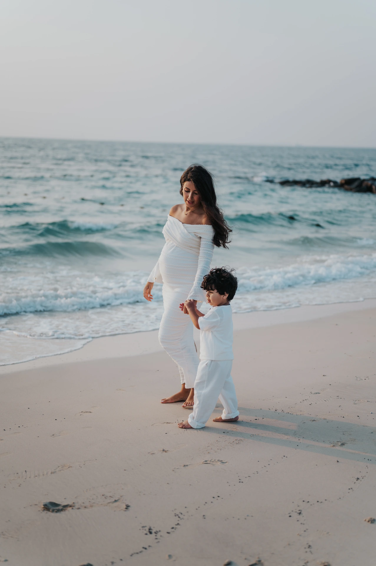 A pregnant mother walks beside her child along the Dubai shoreline during a maternity photoshoot with siblings, capturing a calm and natural family connection.