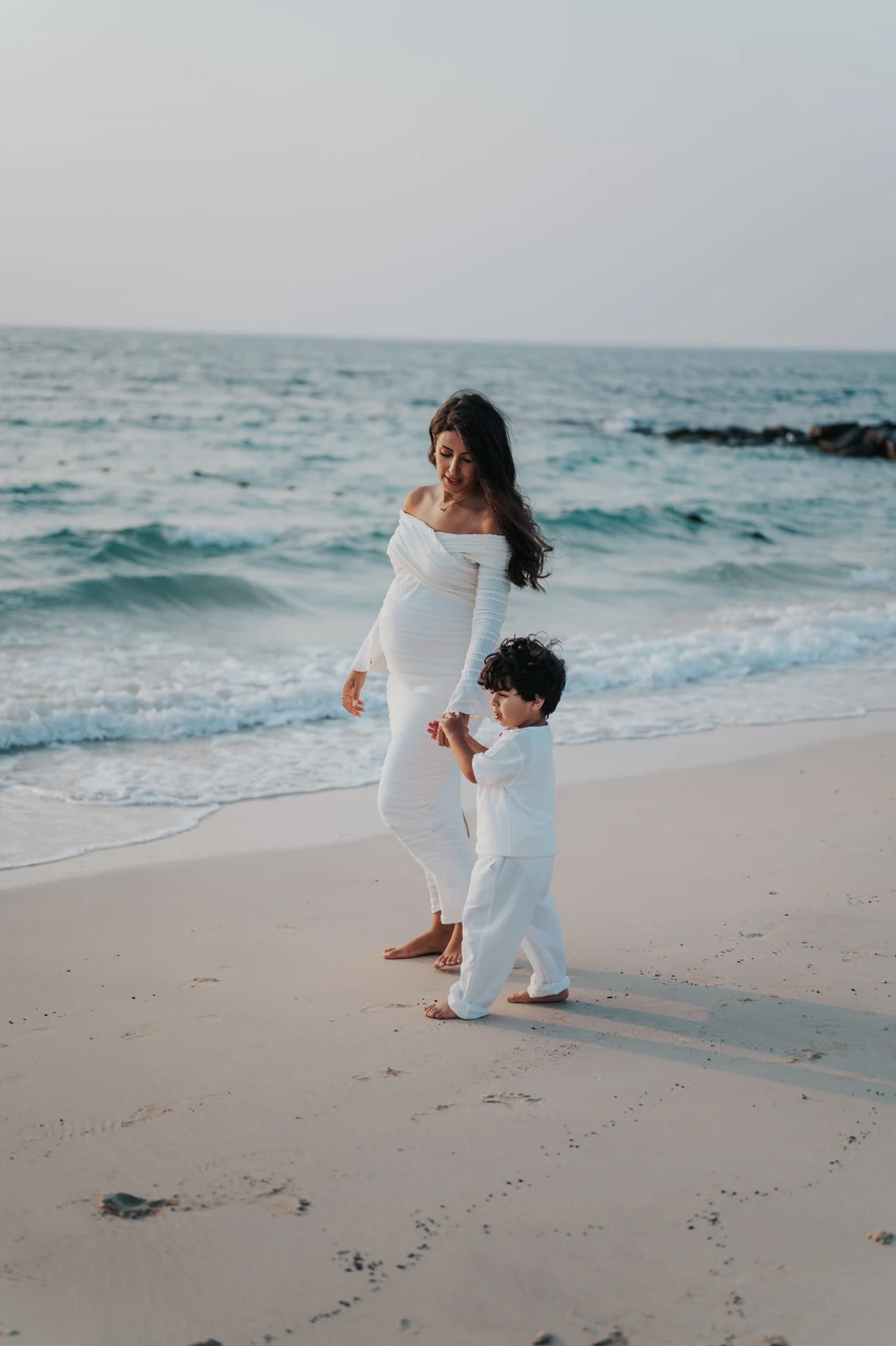 Maternity photoshoot with siblings - mother child shoreline walk A pregnant mother walks beside her child along the Dubai shoreline during a maternity photoshoot with siblings, capturing a calm and natural family connection.