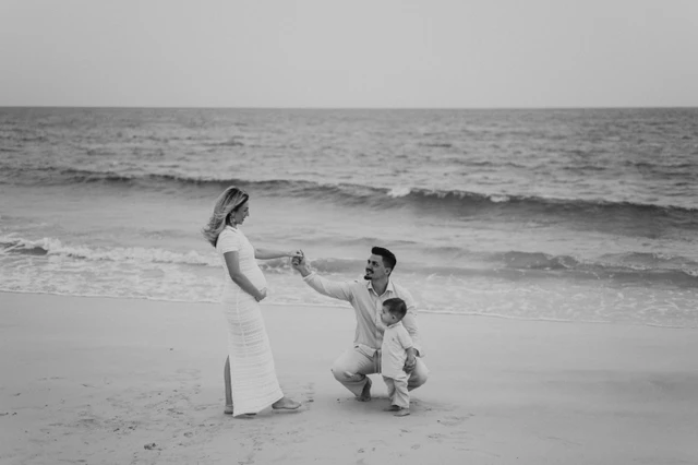 An expecting mother and sibling share a playful shoreline moment with their partner nearby in Dubai during a maternity photoshoot with siblings.