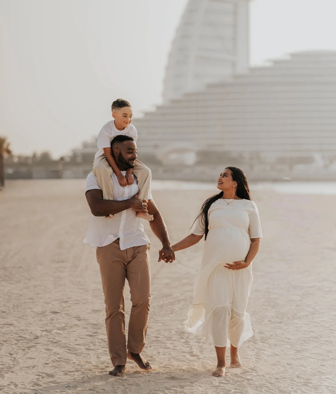 A family walks together on Dubai beach with a child on the father’s shoulders during a maternity photoshoot with siblings and Burj Al Arab backdrop.