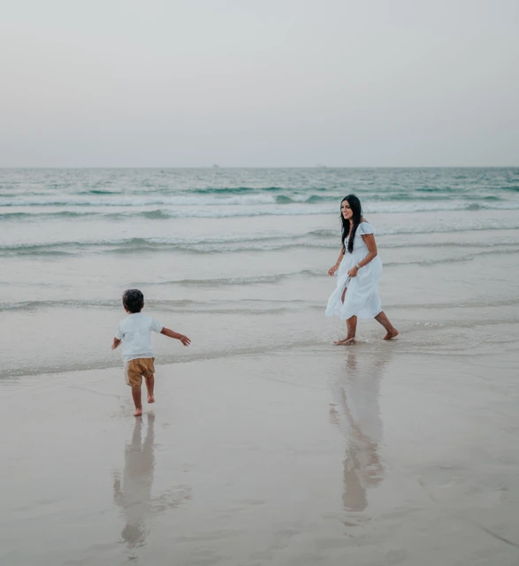 A mother and child play at the Dubai shoreline during a relaxed beach photoshoot with gentle morning waves.