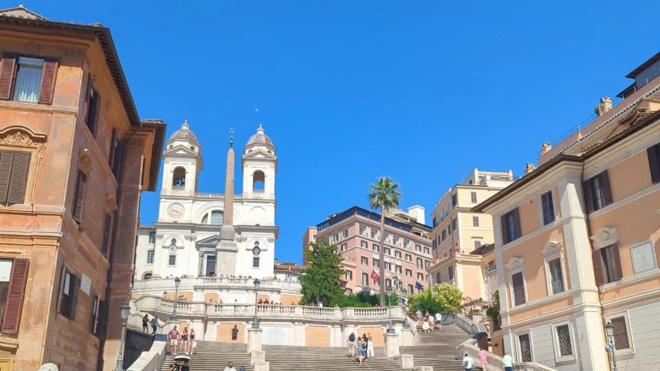 The Spanish Steps rise toward Trinità dei Monti and its obelisk beneath a clear blue sky in central Rome.