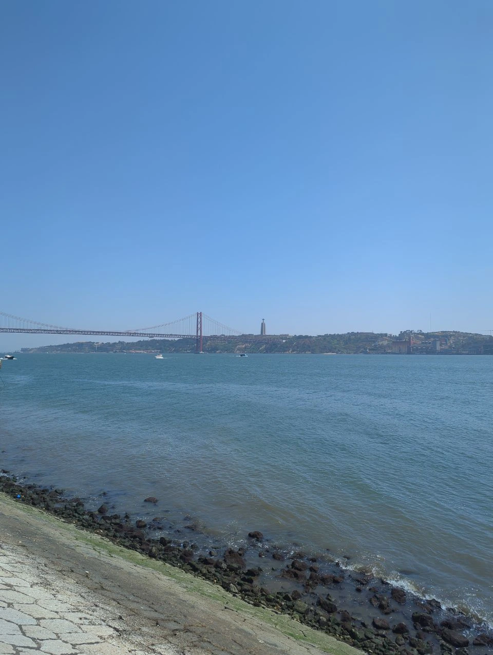 Open water, small boats and the 25 de Abril Bridge stretch across the Tagus beside the Belém riverside walk.