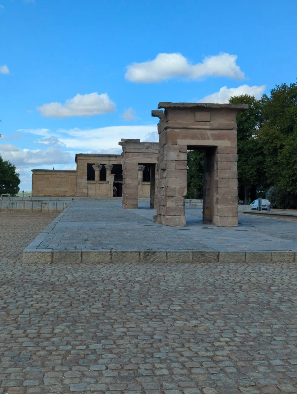 Stone gateways lead towards the Temple of Debod across a cobbled terrace in Madrid, showing its open proposal setting under blue sky.