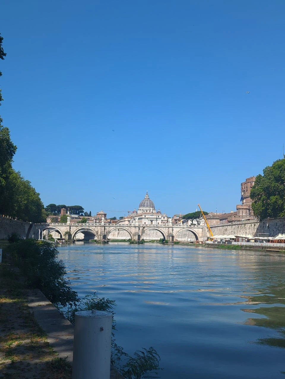 Rome Portrait Photography - Lower Tiber View The Tiber leads toward a stone bridge and St Peter's dome, creating a spacious lower-river view in Rome.