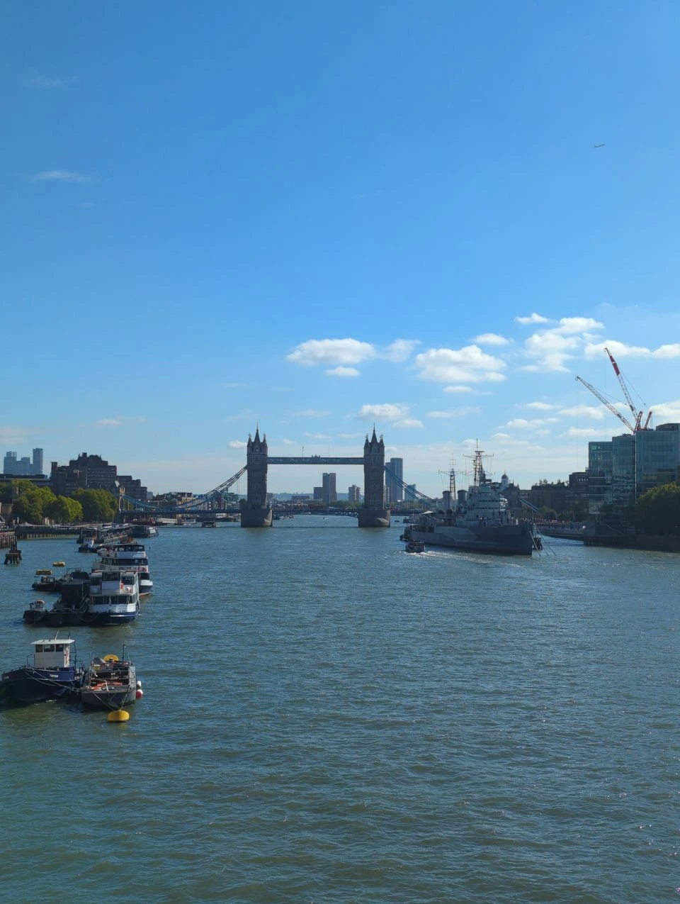 Daytime view east from London Bridge towards Tower Bridge across the Thames, with boats and HMS Belfast