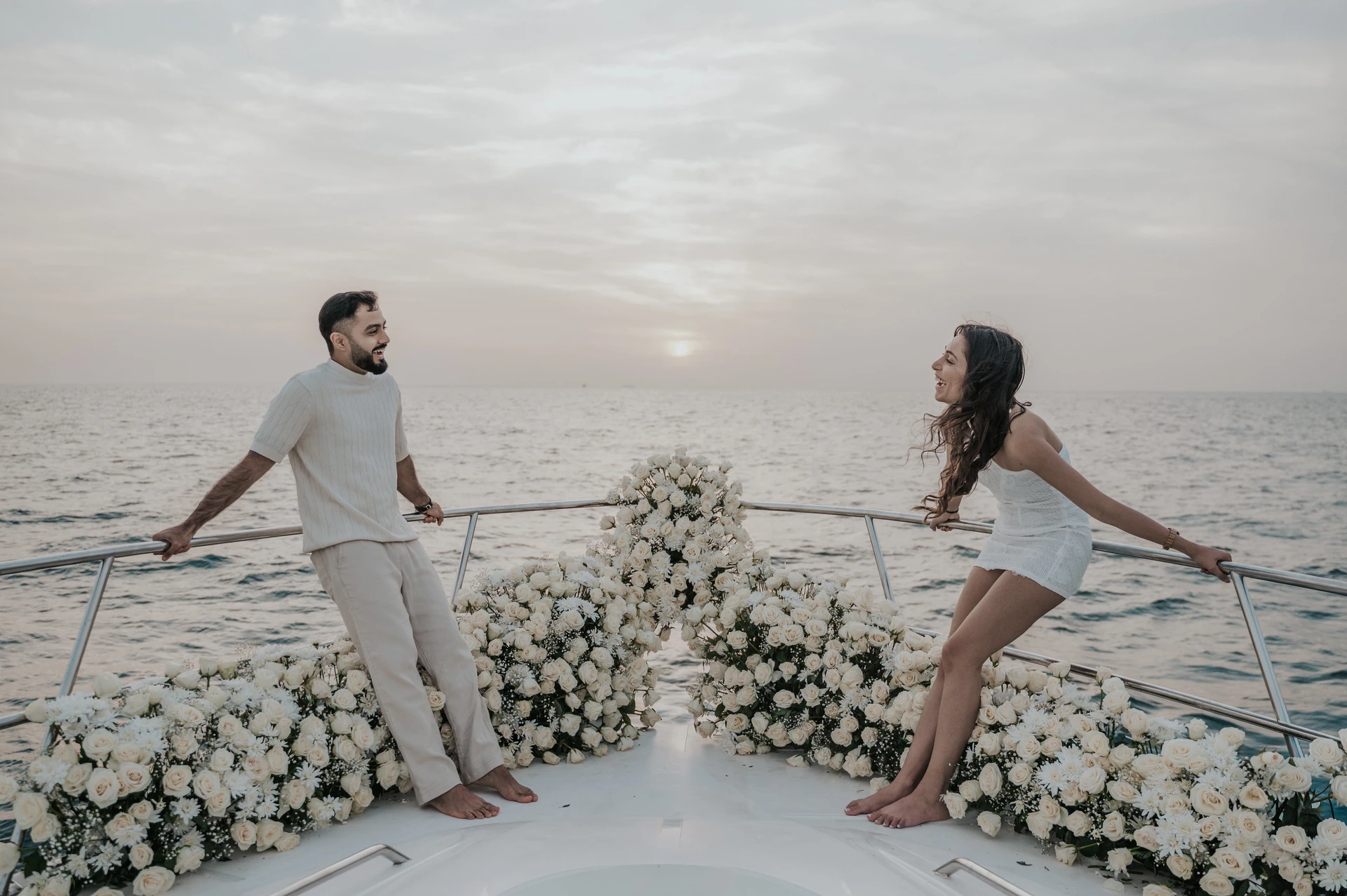 A couple smiles across a flower-lined yacht bow at sunset during their Dubai proposal photographer portrait session.