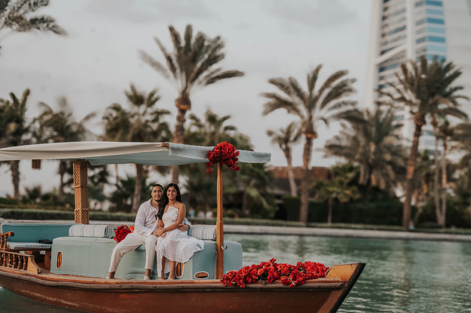 A couple sits on a flower-decorated abra with Burj Al Arab behind them during a Dubai proposal photographer portrait.