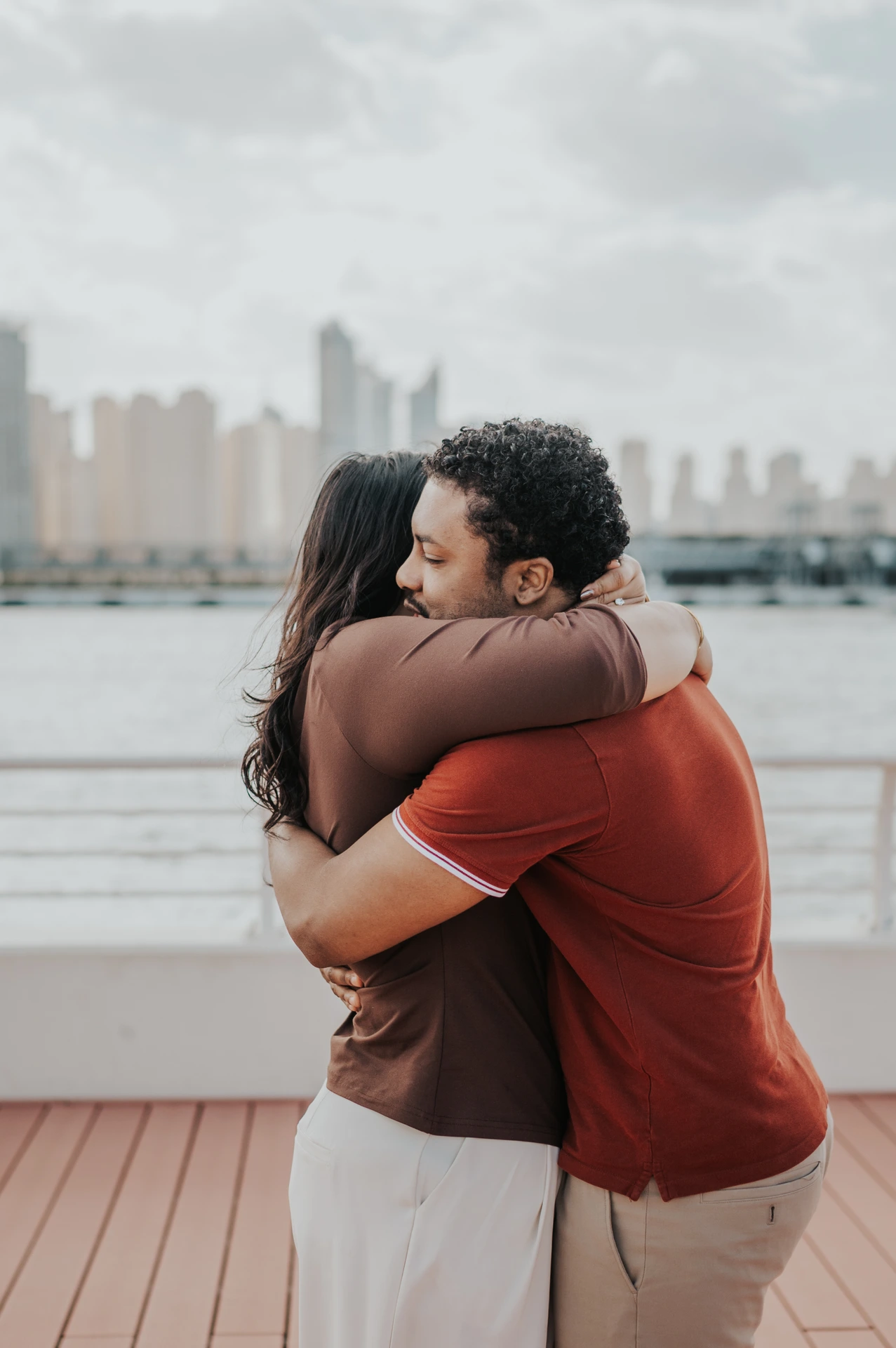 A couple embraces on a yacht deck with a waterfront skyline behind them during their Dubai proposal photography session.