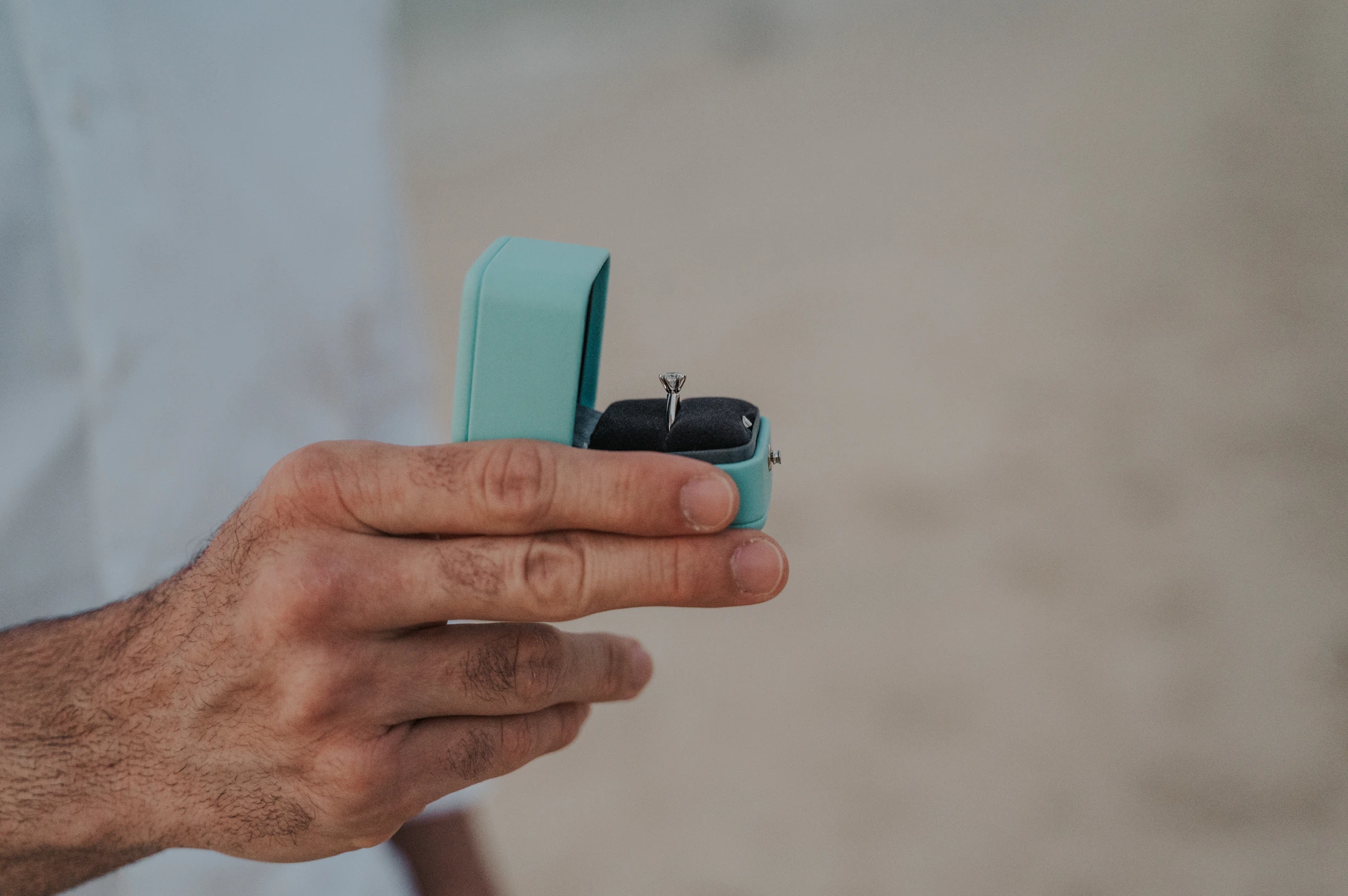 A hand holds an open turquoise ring box with a diamond ring during a Dubai proposal photography detail shot.