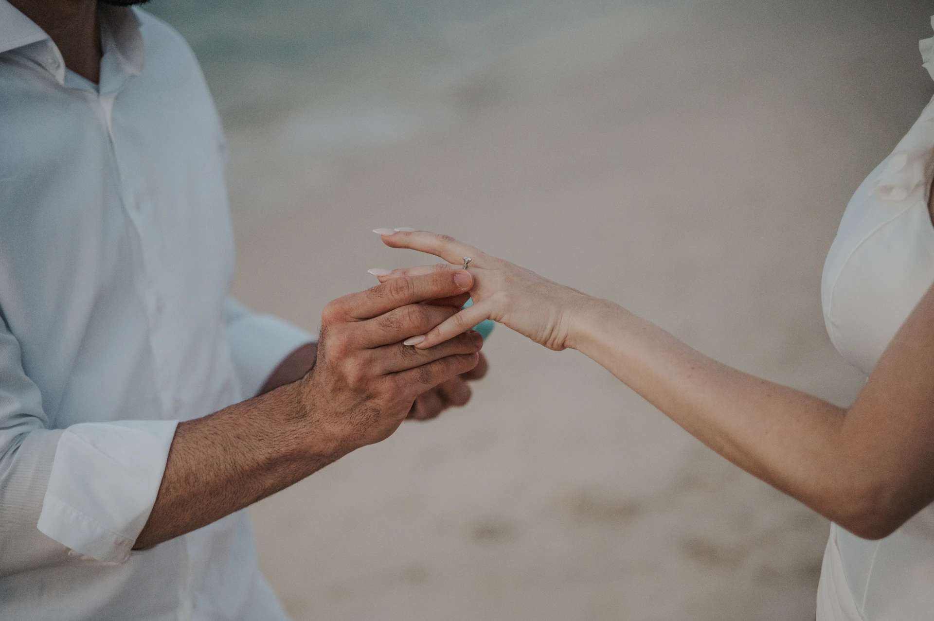 A man slides a ring onto his partner’s finger in a sandy close-up from a Dubai proposal photography session.