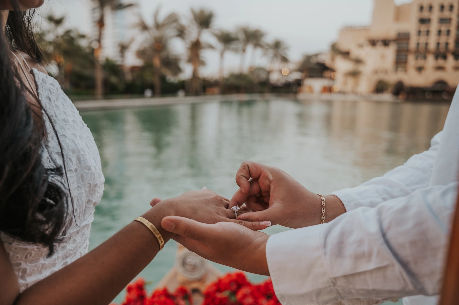 Dubai Canal Proposal Ring Placement A man places an engagement ring on his partner’s finger beside a canal and red roses during a Dubai proposal.