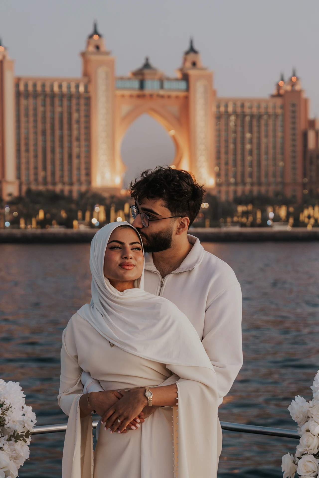 Atlantis Dubai Proposal Forehead Kiss A man kisses his partner’s forehead on a yacht with Atlantis The Palm behind them after a Dubai proposal.