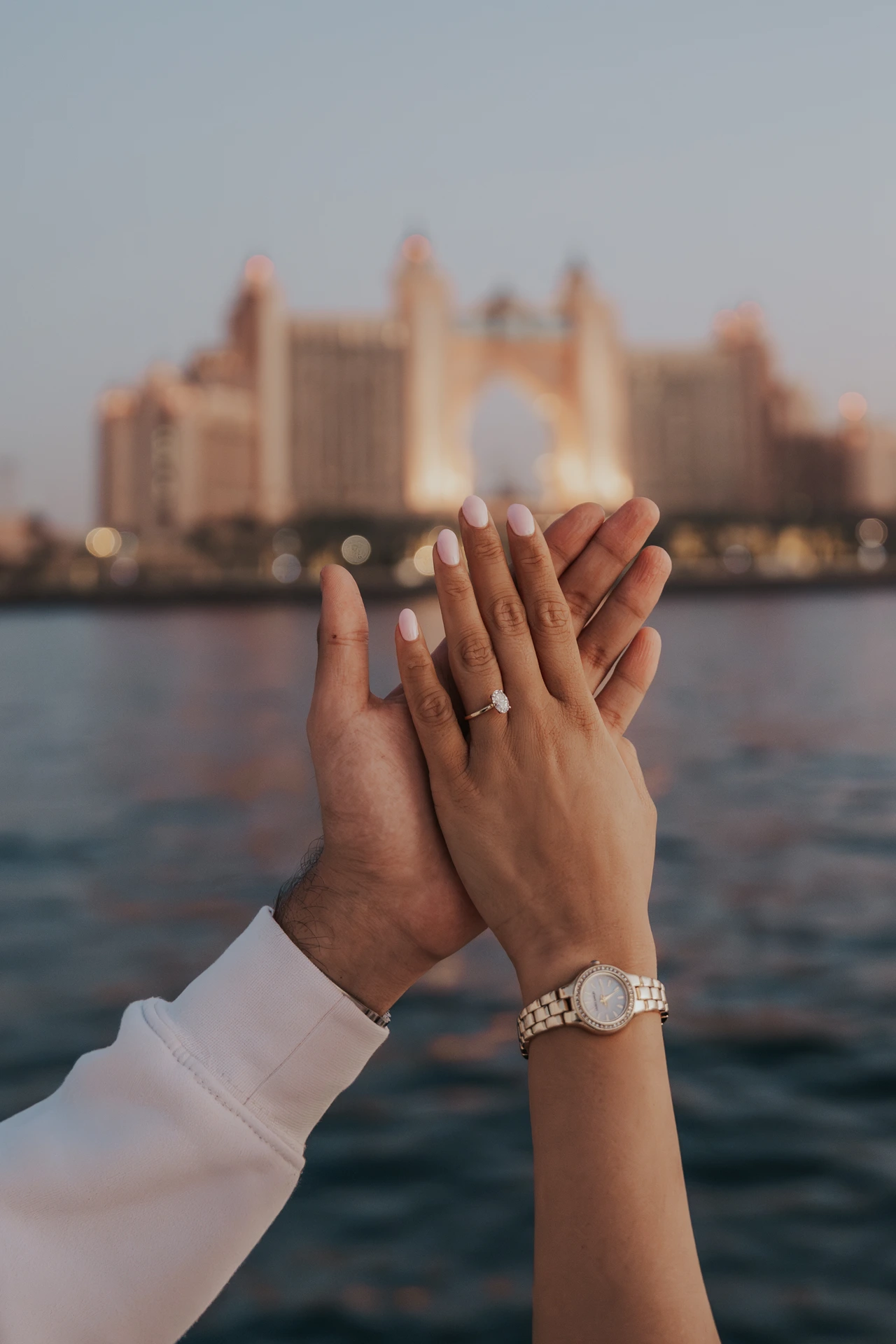 A couple presses their hands together to display an engagement ring with Atlantis The Palm behind their Dubai proposal portrait.