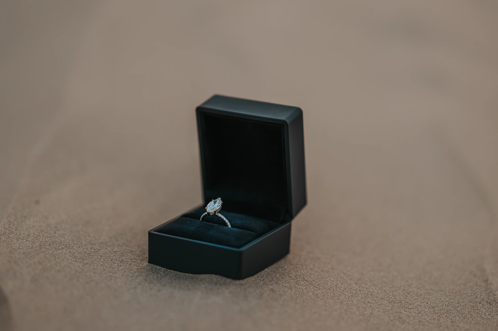 An open black ring box displays a diamond ring on the sand during a Dubai proposal photographer detail shot.