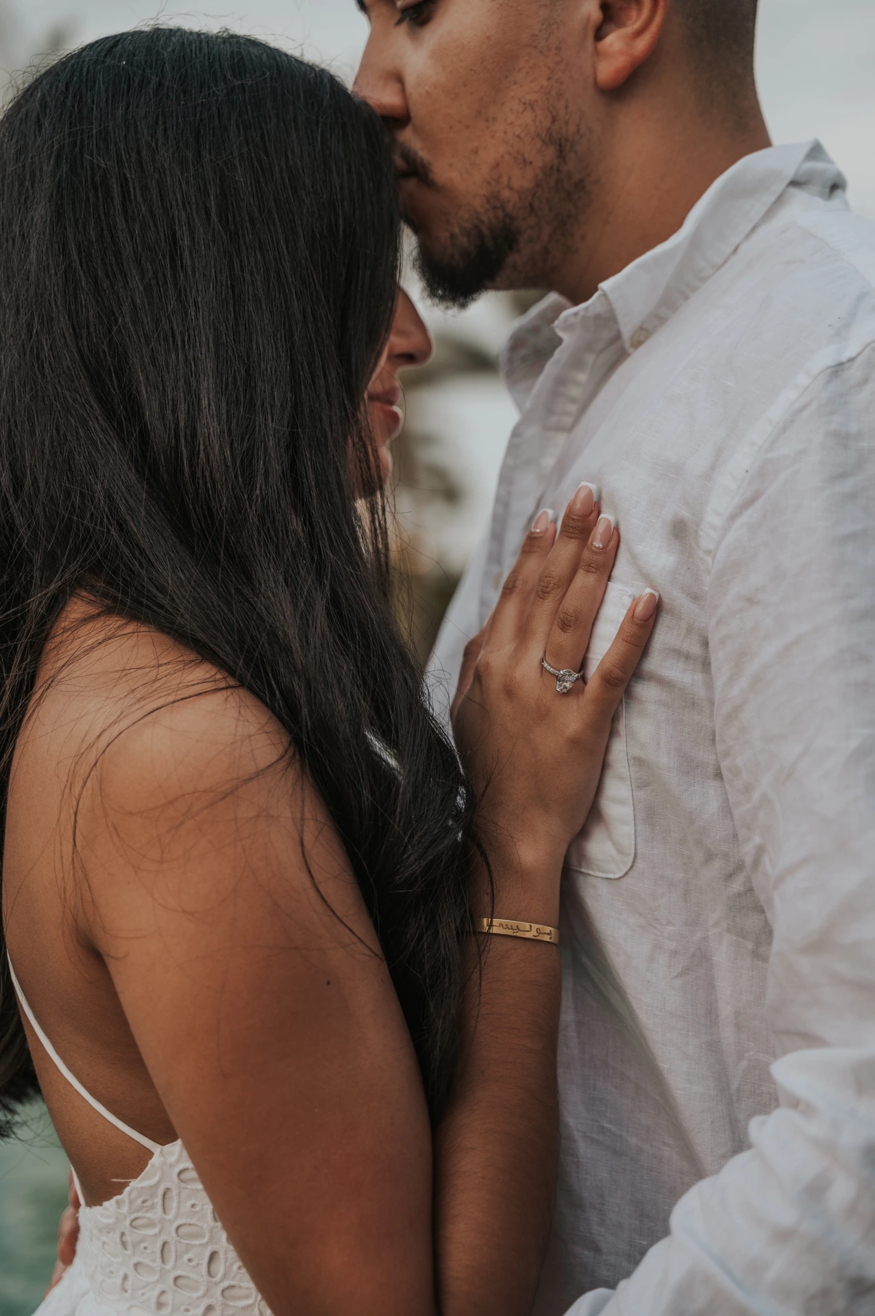 A man kisses his partner’s forehead while she displays her engagement ring during a close-up Dubai proposal portrait.