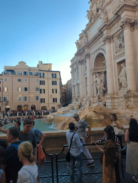 Trevi Fountain and Visitors in Rome Visitors gather beside Trevi Fountain’s turquoise water, sculpted stone facade and surrounding buildings in Rome.