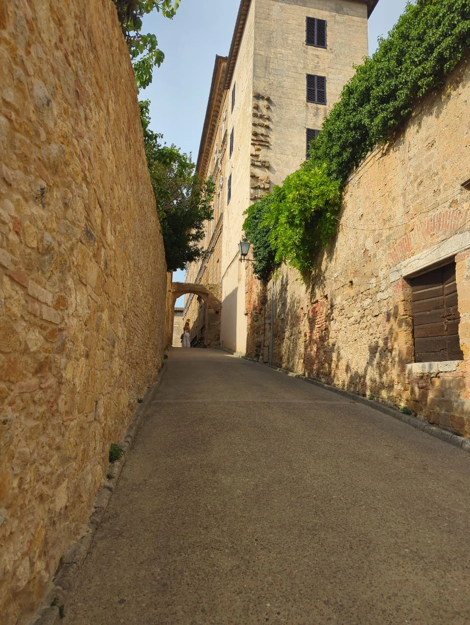 Warm stone lane with greenery and an arch in Pienza, Tuscany