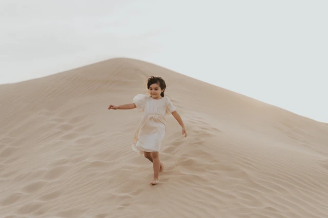A child runs up a Dubai sand dune during a vacation family photoshoot, adding playful movement and candid energy to the family travel gallery.