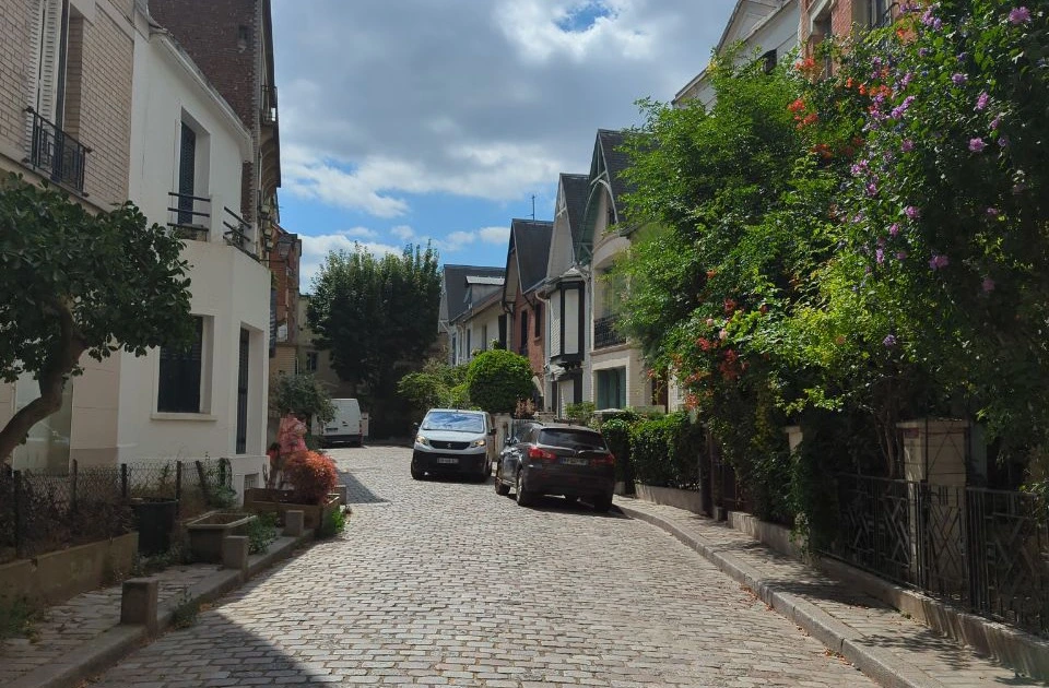 A cobbled lane curves between small houses and flower-covered façades at Villa Léandre, offering a quiet residential setting for a Paris photoshoot.