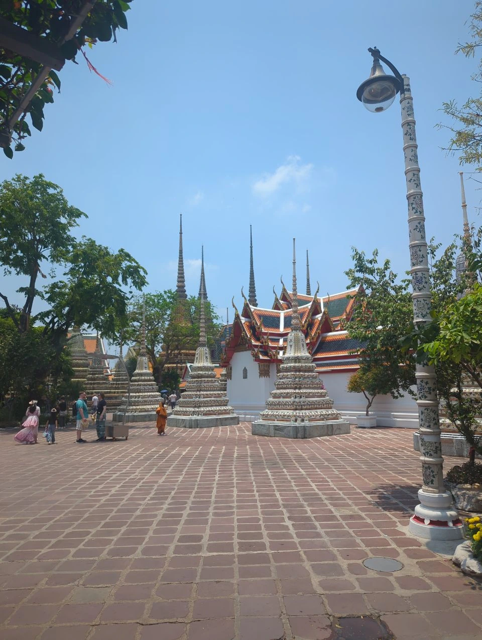 Wat Pho vs Wat Arun Photos - Colourful Courtyard Colourful chedis and tiled temple buildings frame an open courtyard at Wat Pho in Bangkok, with visitors walking through.